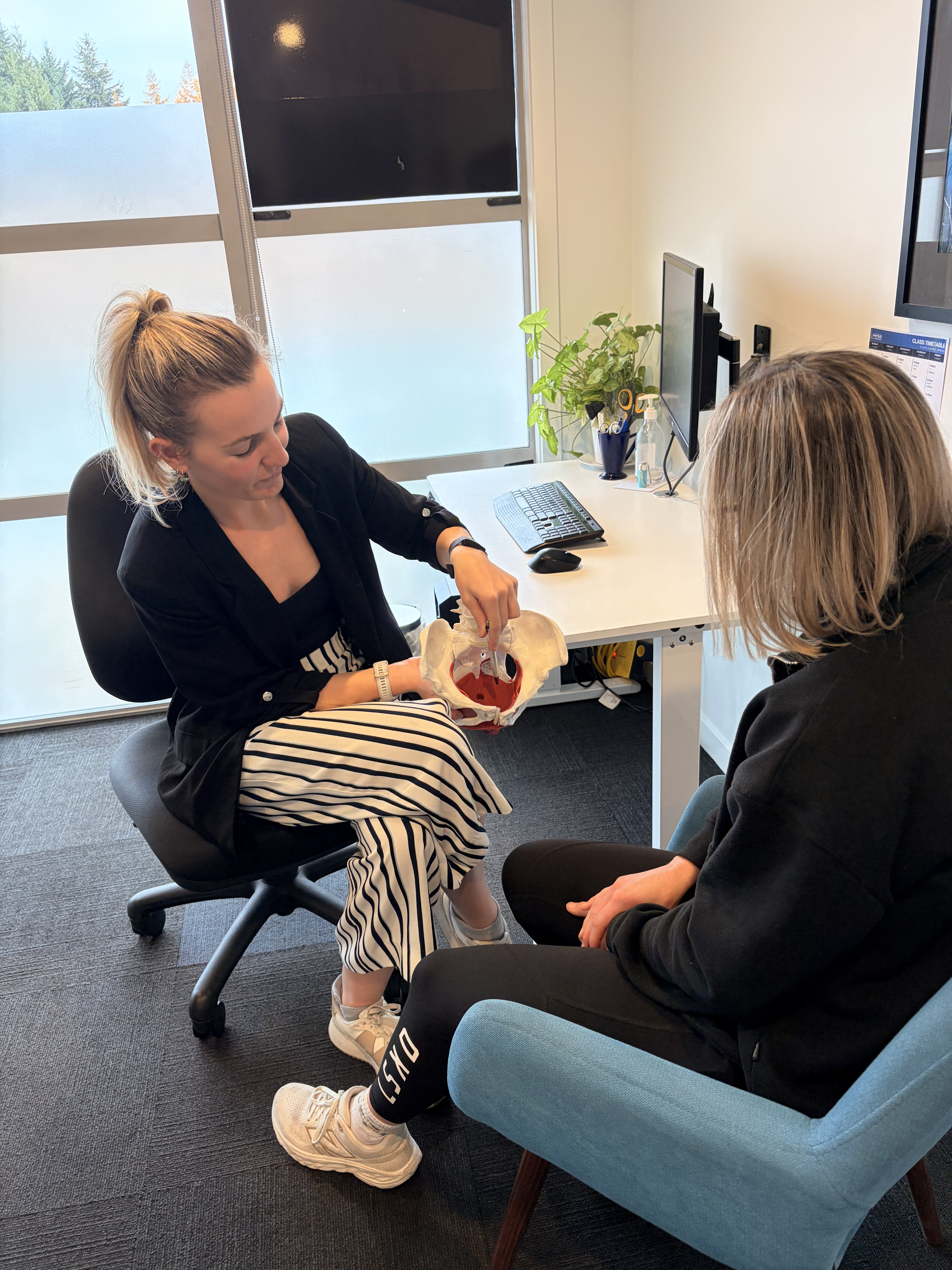 Physiotherapist explaining pelvic floor anatomy using a pelvis model during a consultation